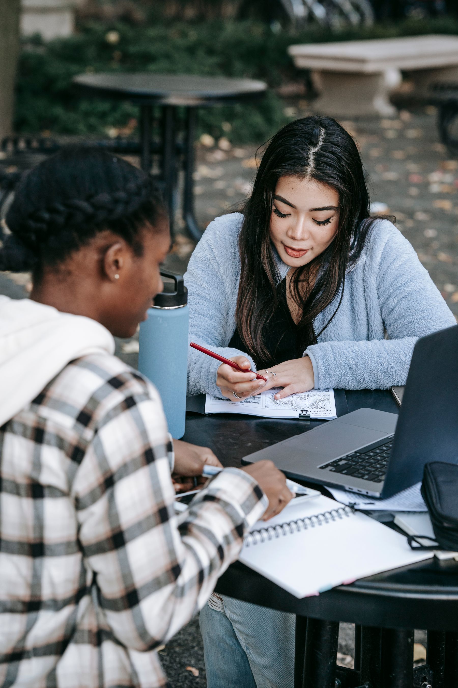 University students discussing research notes beside a laptop at an outdoor table